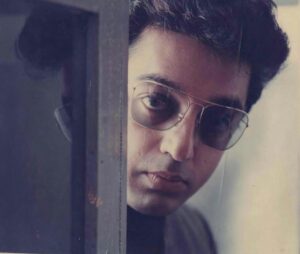Kamal Haasan peers from behind a doorway, wearing tinted glasses, in a contemplative moment from the silent film Pushpak (1987).